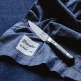 A stainless steel knife is placed on a piece of dark blue fabric with a tag that reads "Wrangler + MADE IN."