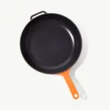 A non-stick frying pan with an orange handle is centered on a light background.