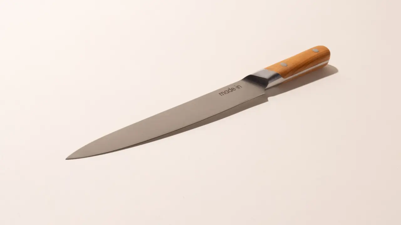 A kitchen knife with a wooden handle and stainless steel blade lies on a neutral background.