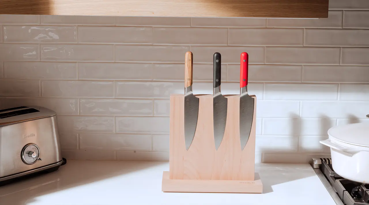 A wooden knife block with three knives on a kitchen counter beside a toaster and near a stove.