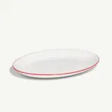A white oval plate with a red rim lies on a plain background.