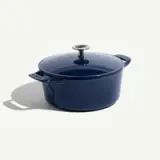 A round, navy blue enameled cast iron Dutch oven with a lid and sturdy handles is displayed against a light background.