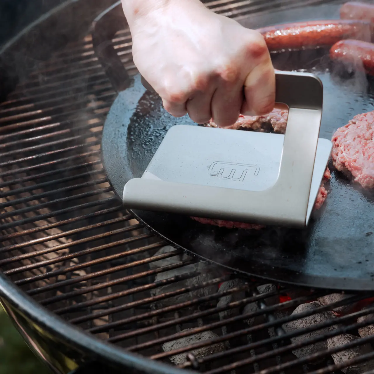 a grill press smashing a burger on a griddle