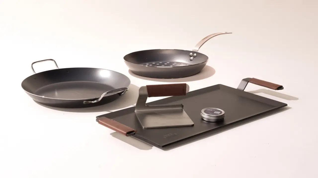 A set of modern cookware and kitchen utensils arranged neatly on a light background.