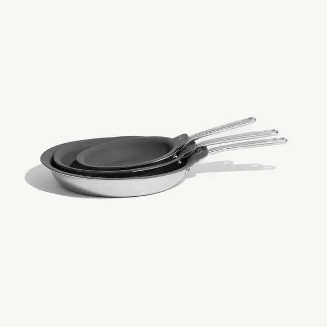 Three non-stick frying pans of different sizes are stacked together with their handles aligned.
