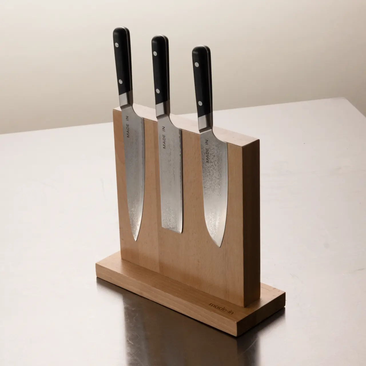 Three chef's knives with black handles are neatly arranged in a wooden knife block on a tabletop.