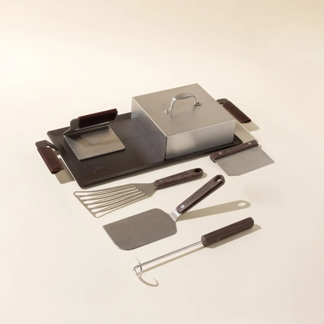 A collection of barbecue tools including a spatula, grilling box, and cleaning brush arranged on a light background.