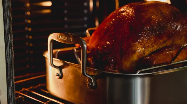 A perfectly roasted turkey sits in a stainless steel roasting pan inside an oven.