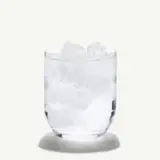 A clear glass filled with ice cubes sits against a light background.