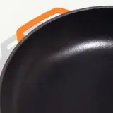 A close-up view of a black non-stick frying pan with an orange silicone handle.