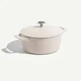 A round, light-colored cast iron pot with handles and a metal lid knob, resting on a white surface.