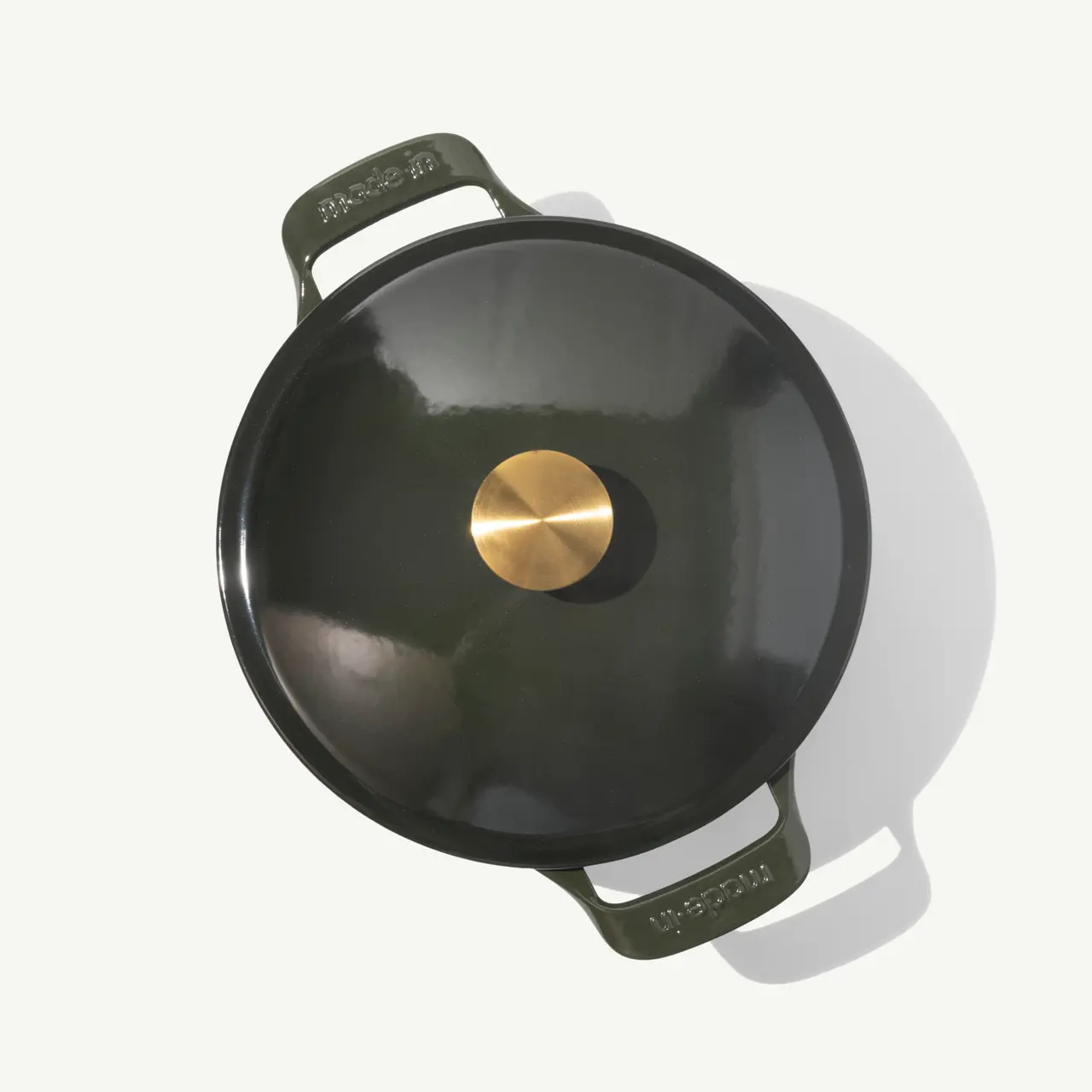 A round, dark green enameled cast iron pot with a brass knob on its lid.