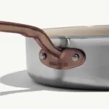 A stainless steel frying pan with a copper handle features a prominent "made-in" label near the handle.