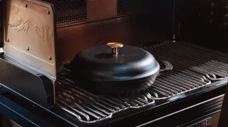 A cast iron skillet rests on a gas grill's grates, ready for outdoor cooking.