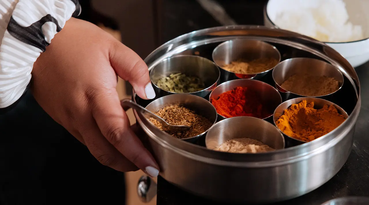 A person holds a spice container with various colorful spices.
