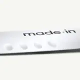 A close-up of a knife blade with the text "made-in" engraved on it, showing four hollow indentations.