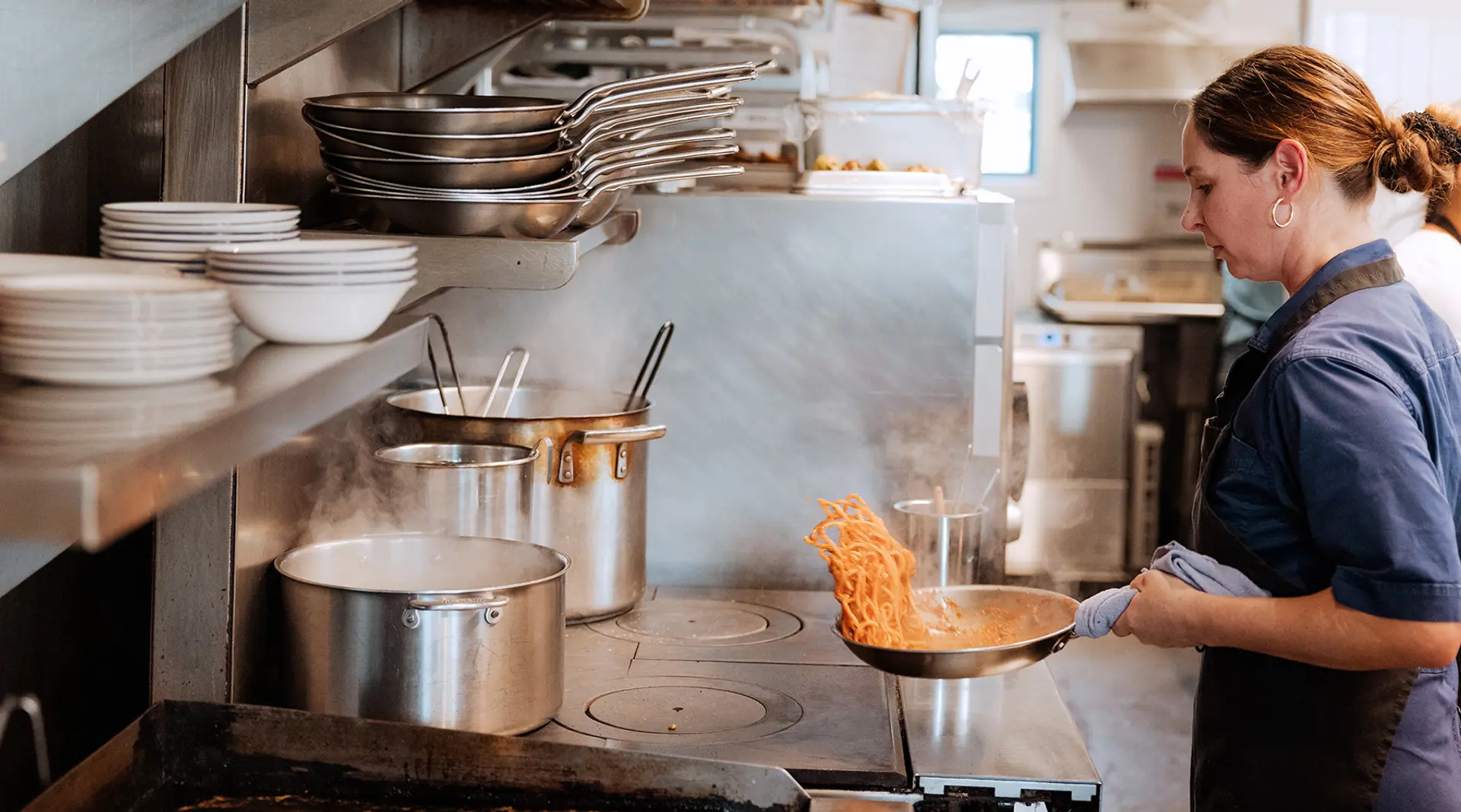 A chef is cooking pasta in a large, industrial kitchen.