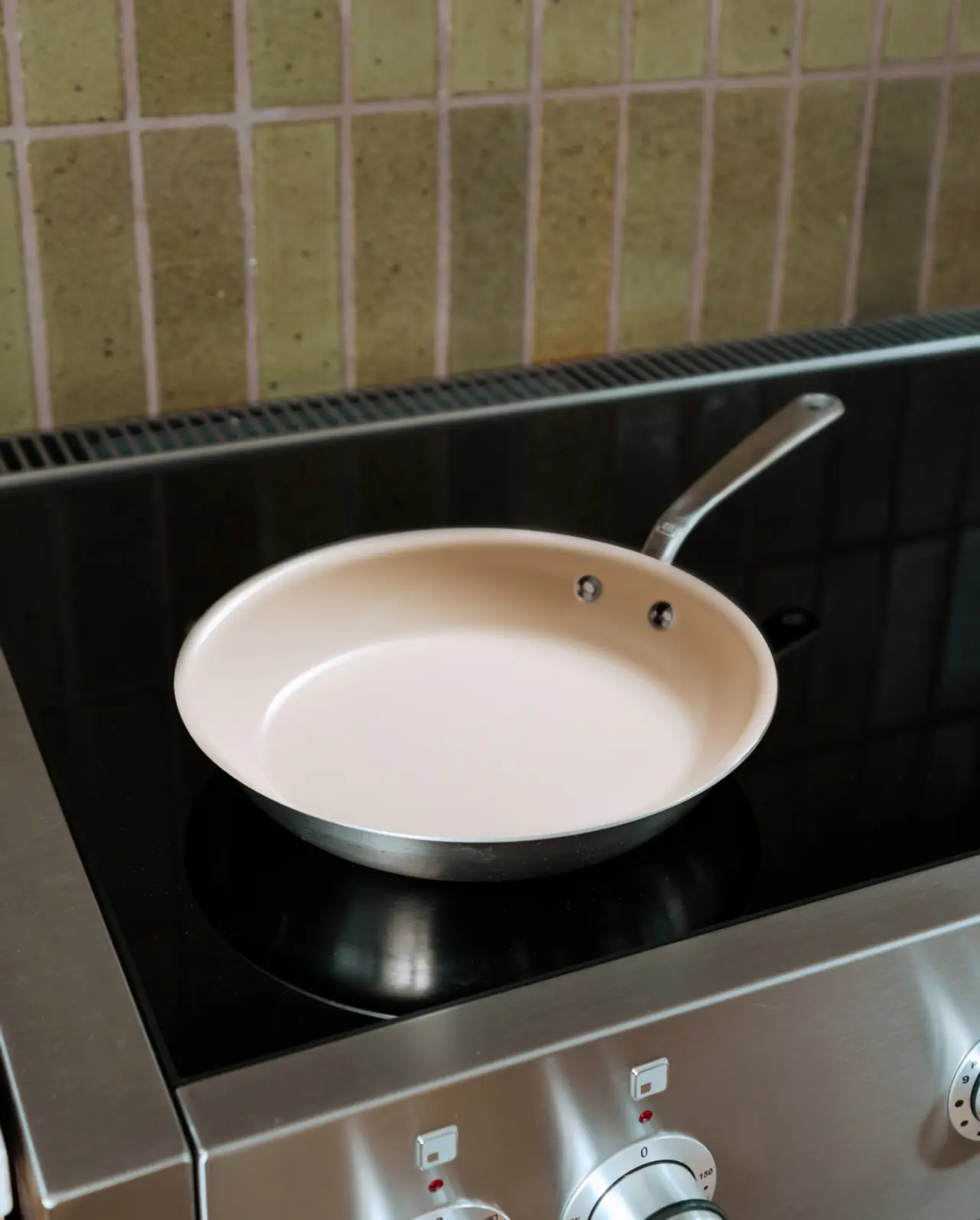 A frying pan rests on a modern stovetop with tiled backsplash in the background.