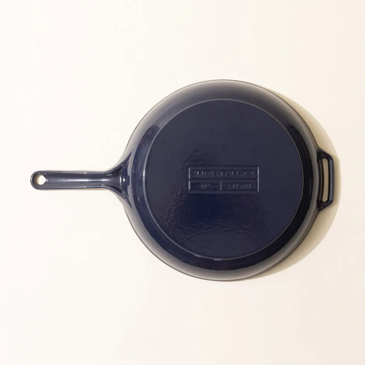 A navy blue cast iron skillet with a handle and an opposite side grip lies against a plain background.