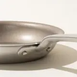 Close-up side view of a modern frying pan with a silver handle on a light background.