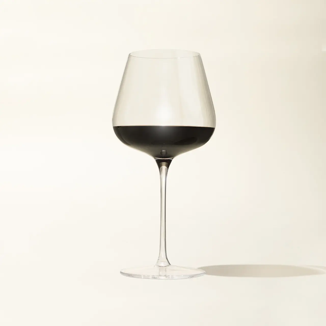 A wine glass filled with red wine is displayed against a plain beige background.