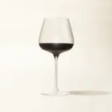 A wine glass filled with red wine is displayed against a plain beige background.