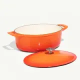 A vibrant orange enameled cast iron Dutch oven with its lid placed to the side on a light background.