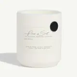 White minimalist candle with a label describing its scent and burn time.