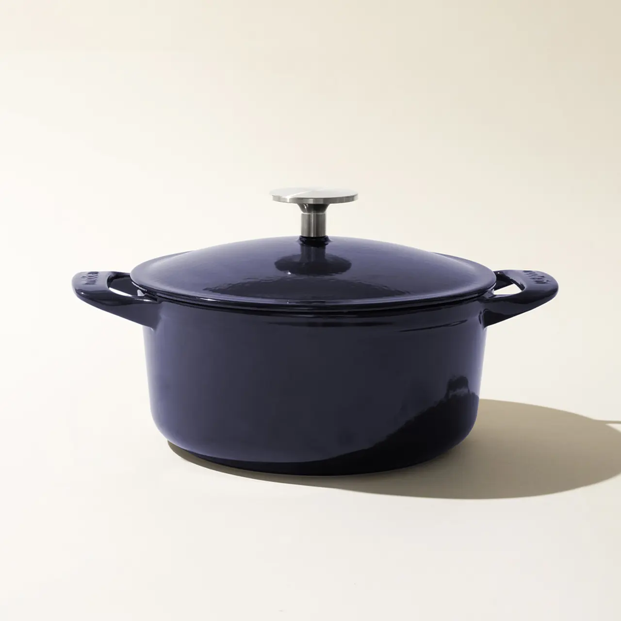 A navy blue enameled cast iron Dutch oven with a lid, set against a beige background.