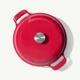 A bright red cast iron pot with a stainless steel knob sits against a light background.