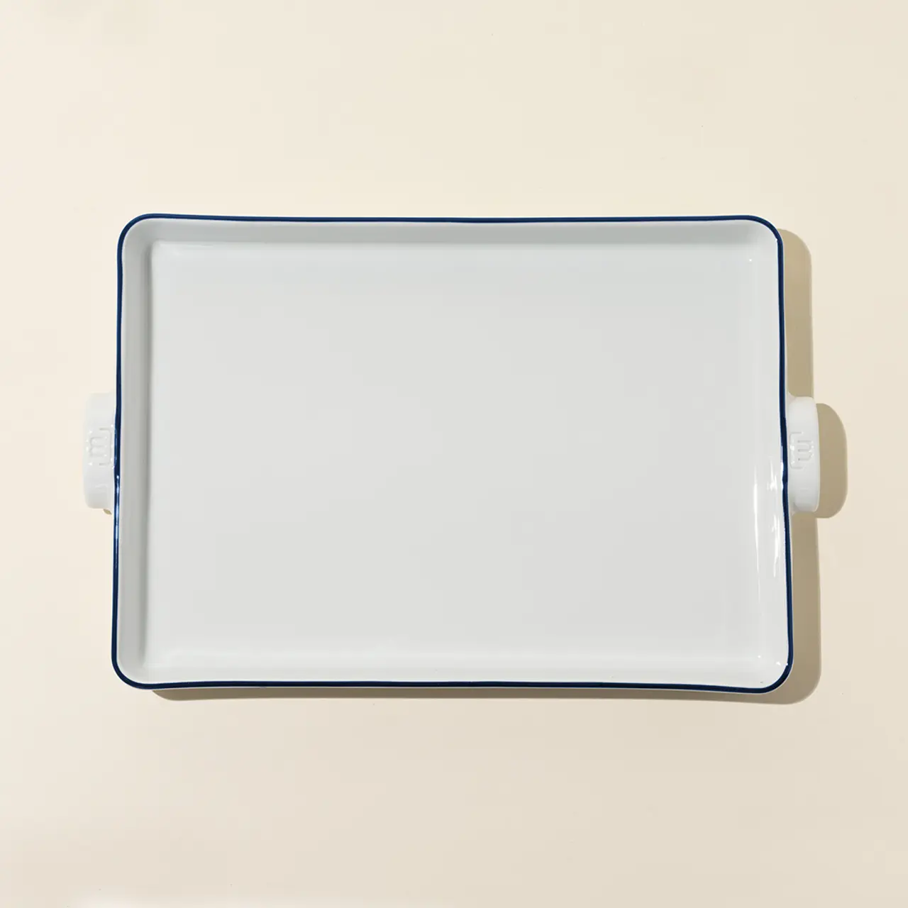 A white square plate with a blue rim and small handles on two sides sits on a plain surface.