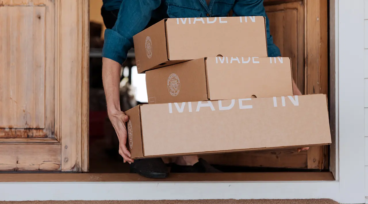 A person carries multiple cardboard boxes labeled "MADE IN" out of a wooden structure.