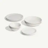 Stacked white ceramic plates and bowls are arranged on a plain background.