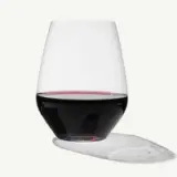 A stemless wine glass filled with red wine casts a shadow on a light background.