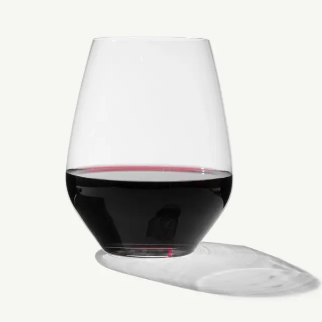 A stemless wine glass filled with red wine casts a shadow on a light background.