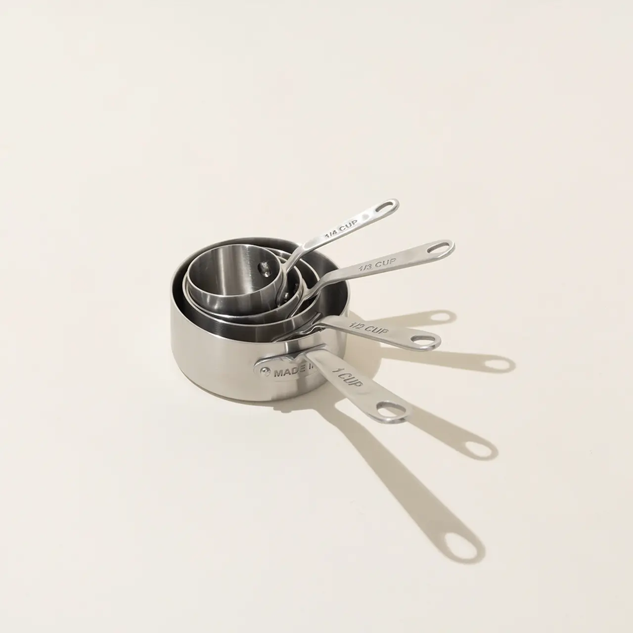 A set of metal measuring cups with handles is neatly stacked on a light surface.