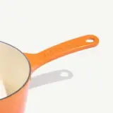 An orange measuring cup with a handle and visible measurement markings is set against a light background.