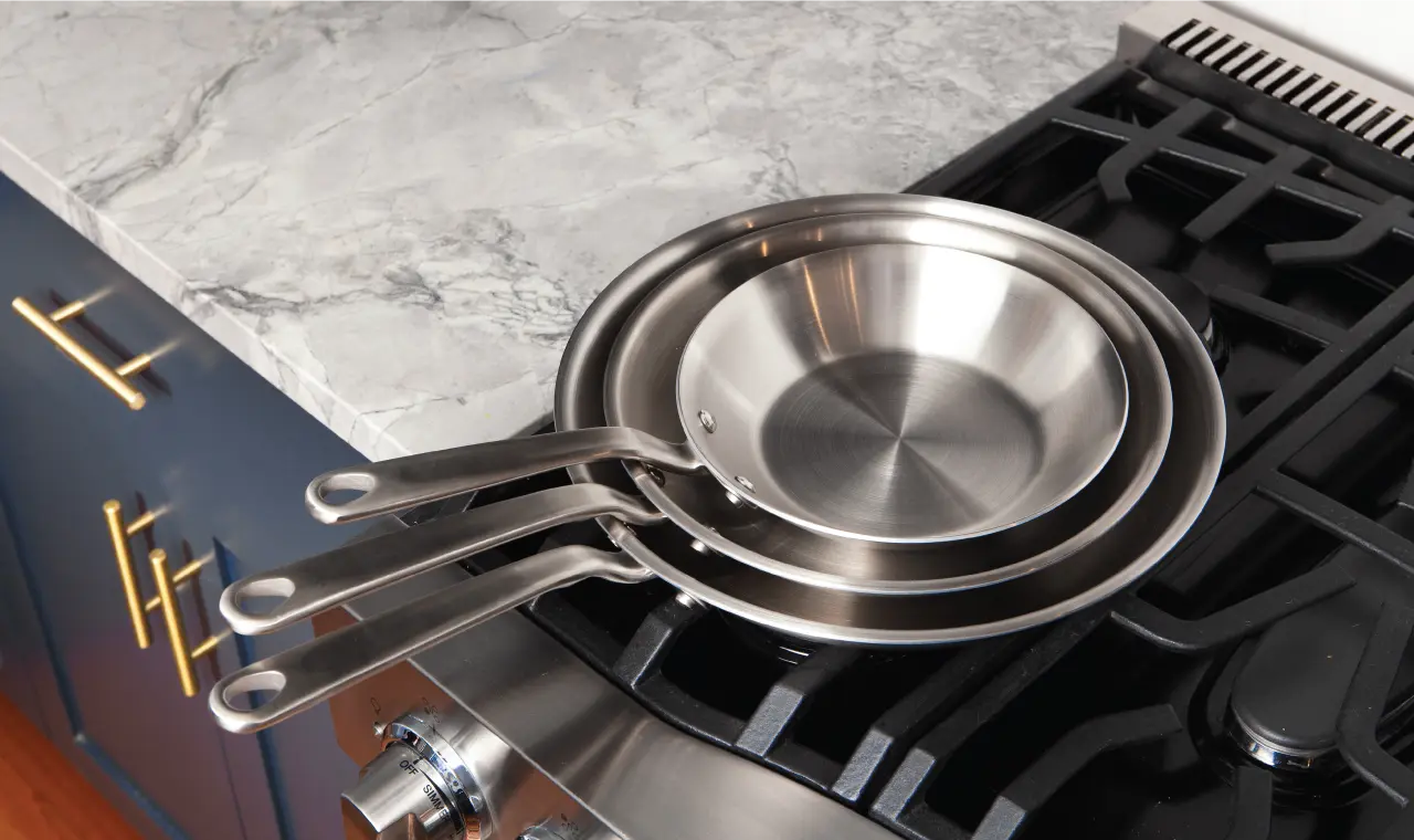 A set of stainless steel pans on a modern gas stove top with a marble countertop background.