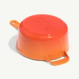 An overturned orange plastic container with two handles is resting on a white surface.