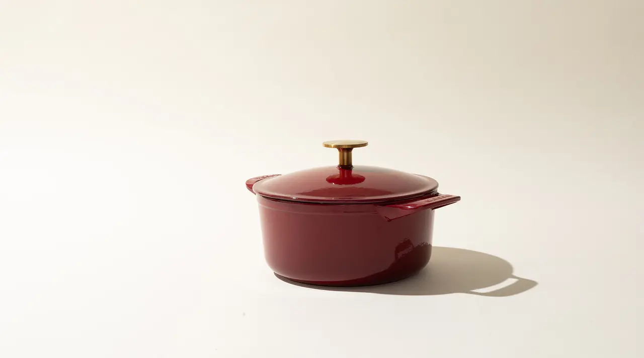 A red enameled cast iron Dutch oven with a lid, set against a neutral background.
