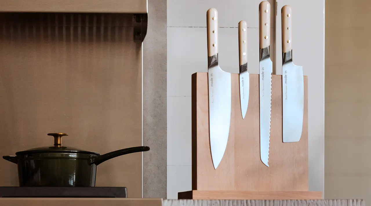 A wooden knife block on a countertop holds four large kitchen knives next to a stove with a pot on it.