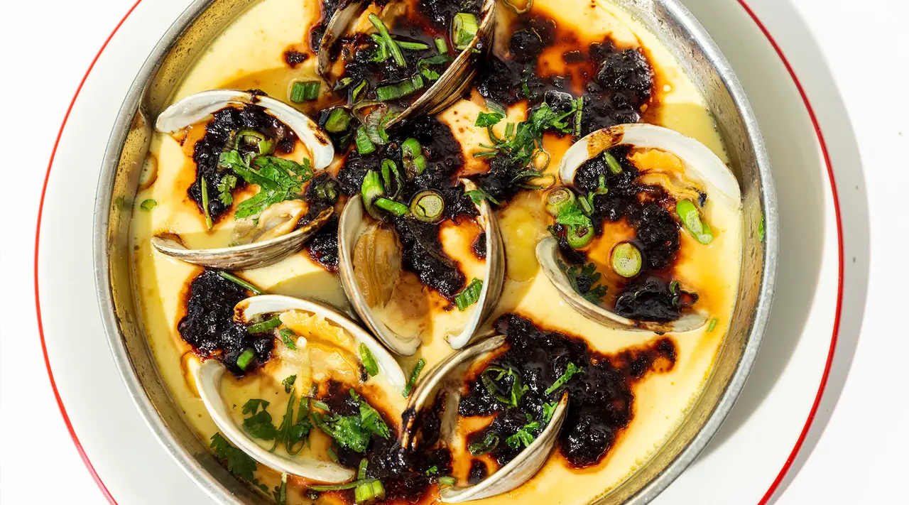 Clams are served in a creamy sauce topped with green onions and a dark, caramelized topping.