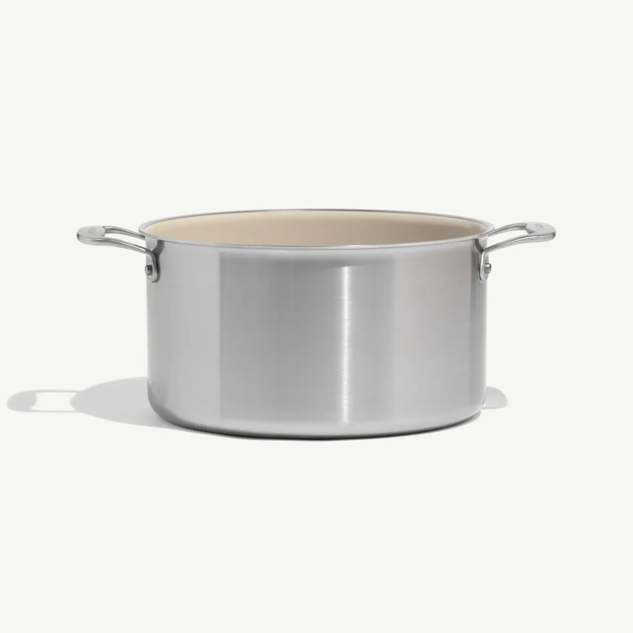 A stainless steel pot with two handles and a light-colored interior sits on a soft background.