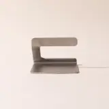 A minimalist metal object with a curved top and a flat base, possibly functioning as a desk lamp or a decorative piece.