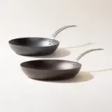 Two black non-stick frying pans with silver handles arranged diagonally on a light background.