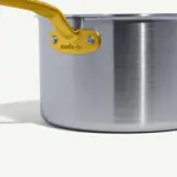 A stainless steel saucepan with a bright yellow handle displays a "made-in" tag.