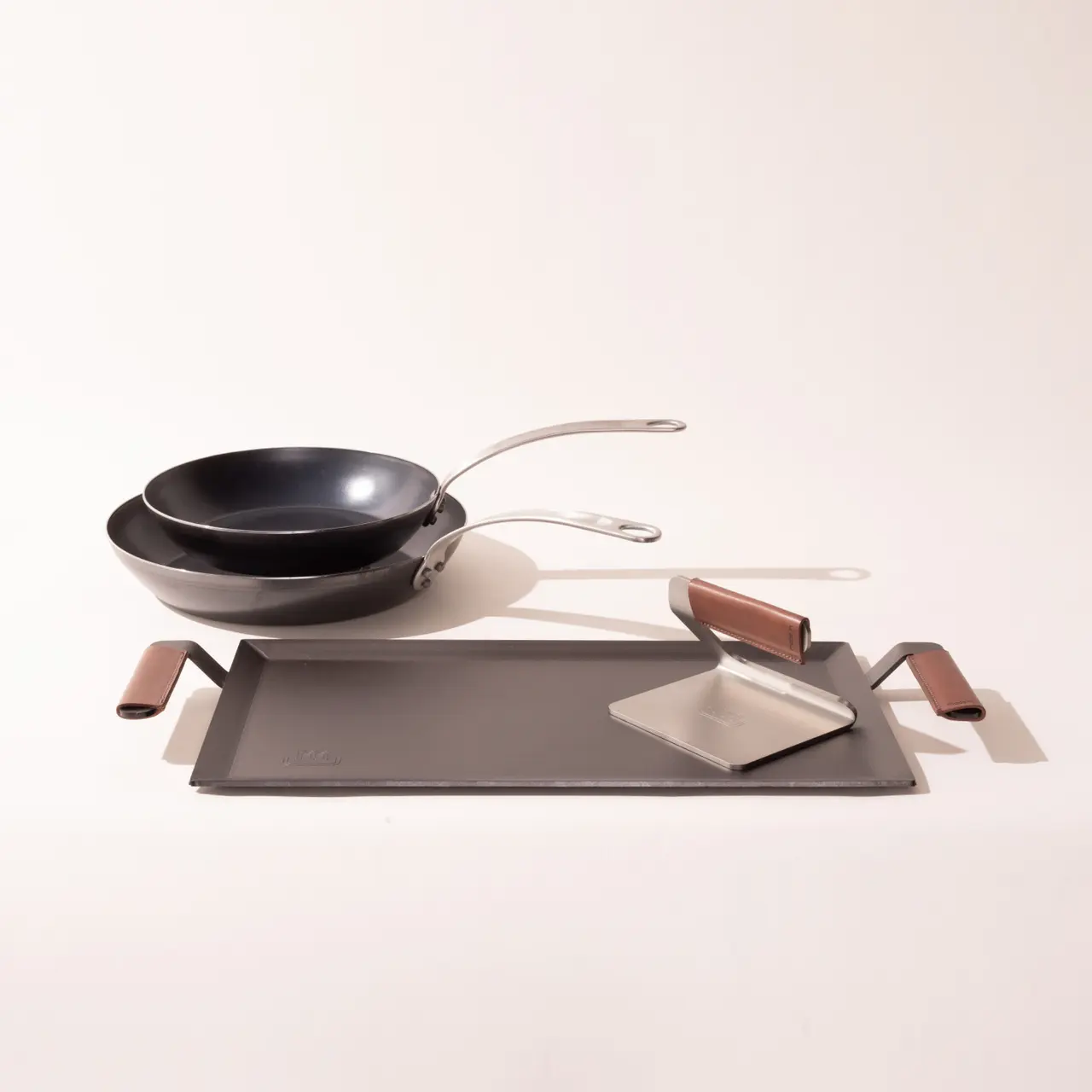 Two pans are positioned on a flat surface alongside a spatula and a pair of pot holders.