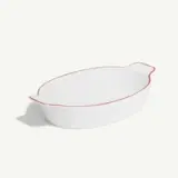 A white oval ceramic baking dish with a slightly flared rim and red trim.