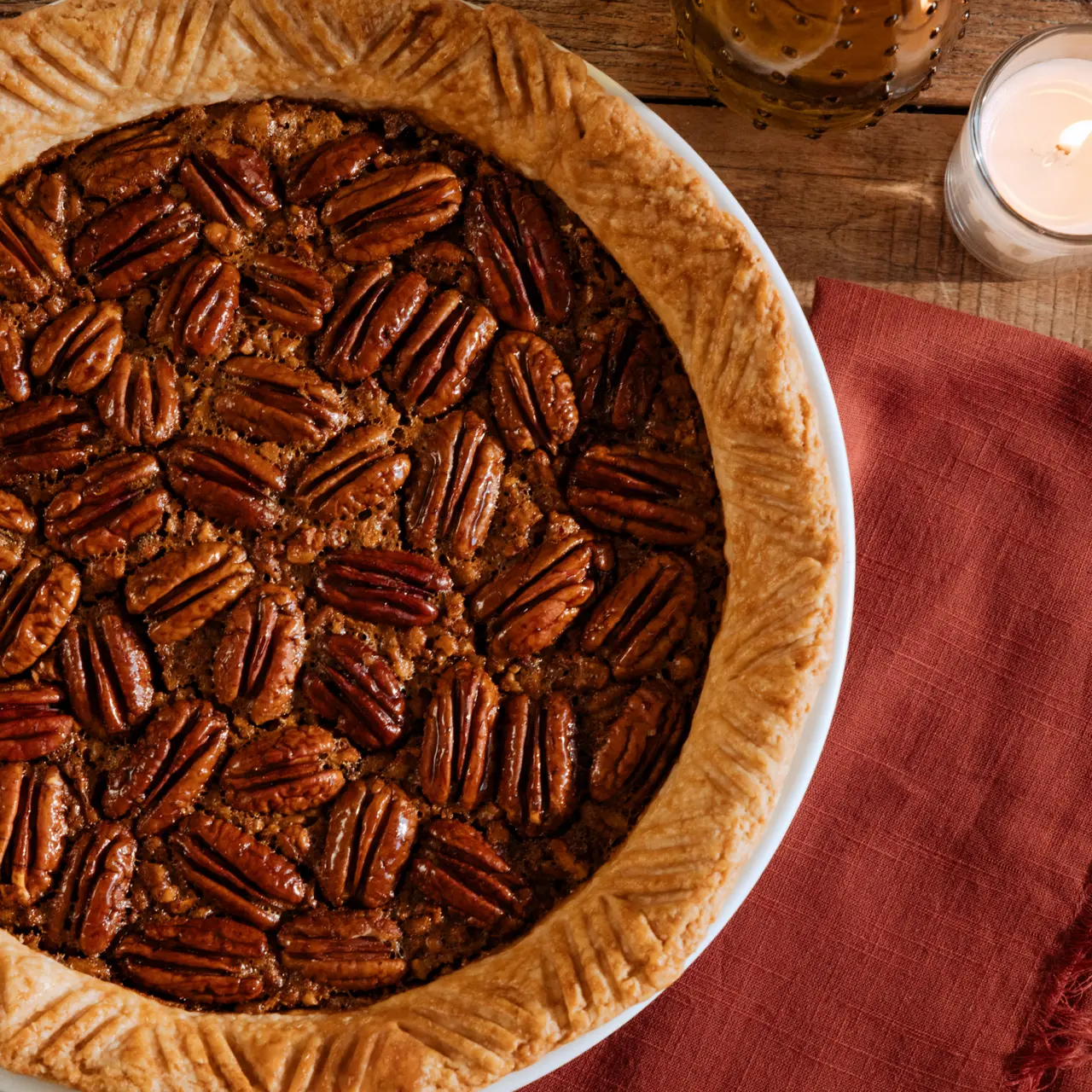 A freshly baked pecan pie is placed on a wooden surface, showcasing a crust and a decorative arrangement of pecans on top.