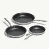 Three different sized non-stick frying pans with metal handles are arranged on a white surface.